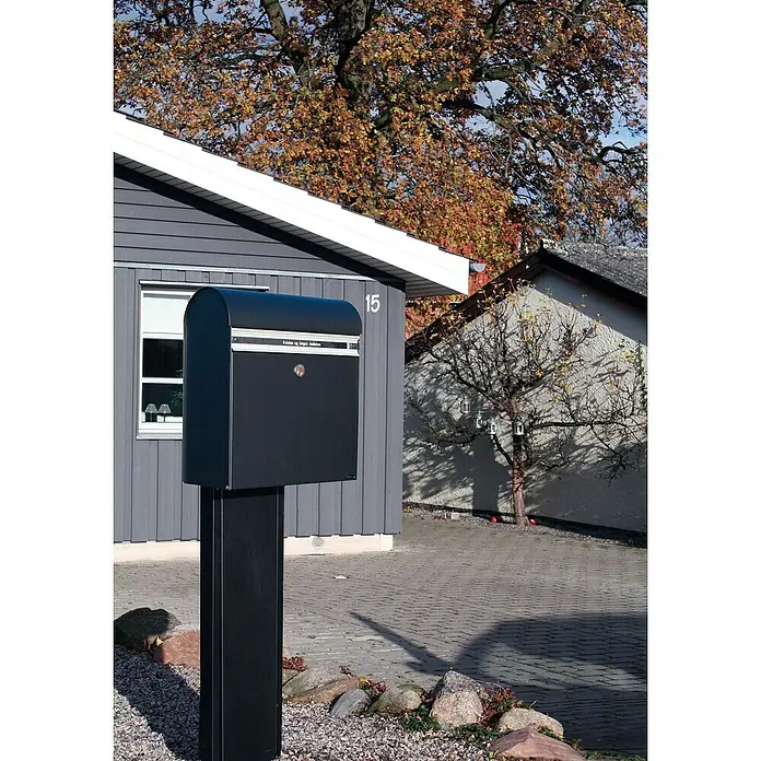 Allux Standbriefkasten KS200 - L x B x H: 170 x 400 x 445 mm, Schwarz, Stahl, Namensschild - Schwarzer Briefkasten mit Ständer vor einem Haus mit grauer Fassade. Der Briefkasten ist modern und schlicht gestaltet, ideal für den Außenbereich.