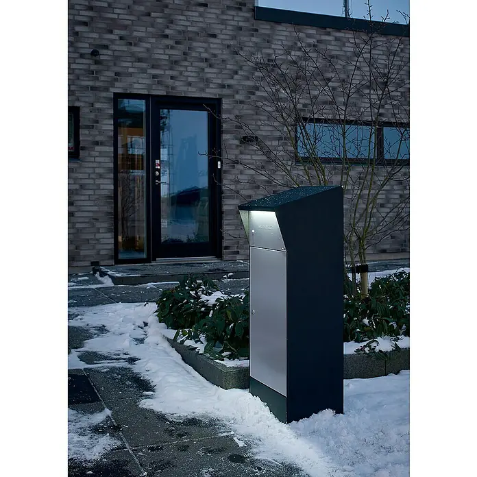 Allux Paketbox Björn mit LED - L x B x H: 365 x 400 x 1.100 mm, Schwarz / Grau, Stahl, Paketfach - Moderne Briefkastenanlage in Schwarz und Silber vor einem Haus im Winter. Der Briefkasten ist mit einer integrierten Beleuchtung ausgestattet.
