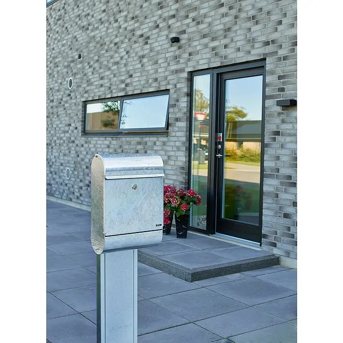 Allux Standbriefkasten 9000 - L x B x H: 165 x 340 x 500 mm, Silber, Stahl - Silberner Briefkasten auf einem Sockel vor einem modernen Haus mit grauer Backsteinfassade.