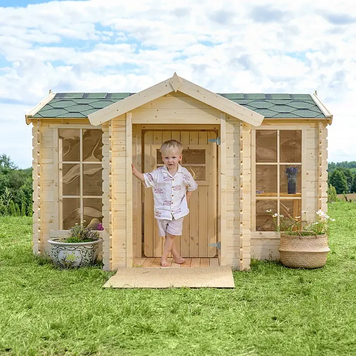 Timbela Spielhaus - L x B x H: 187 x 241 x 151 cm, Holz, Natur - Niedlicher Junge vor einem Holzspielhaus mit grünem Dach. Das Haus steht auf einer grünen Wiese und ist mit Blumen geschmückt.