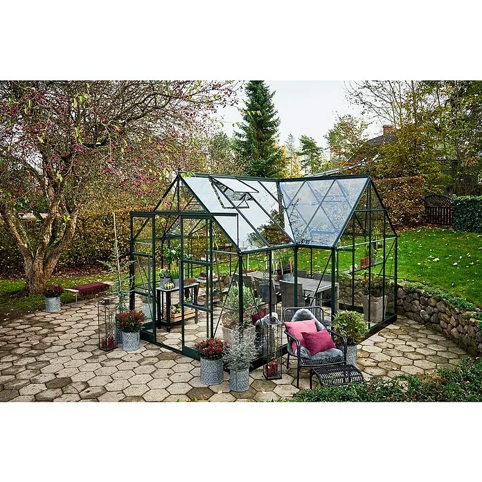Halls Gewächshaus Icon Gardenhouse - Außenmaß inkl. Dachüberstand (B x T): 383,9 x 381,5 cm, Material Seitenwand: Glas, 3 mm, Grün - Das Bild zeigt ein Gewächshaus mit einer Inneneinrichtung mit Tisch und Stühlen in einem Garten mit Steinterrasse.