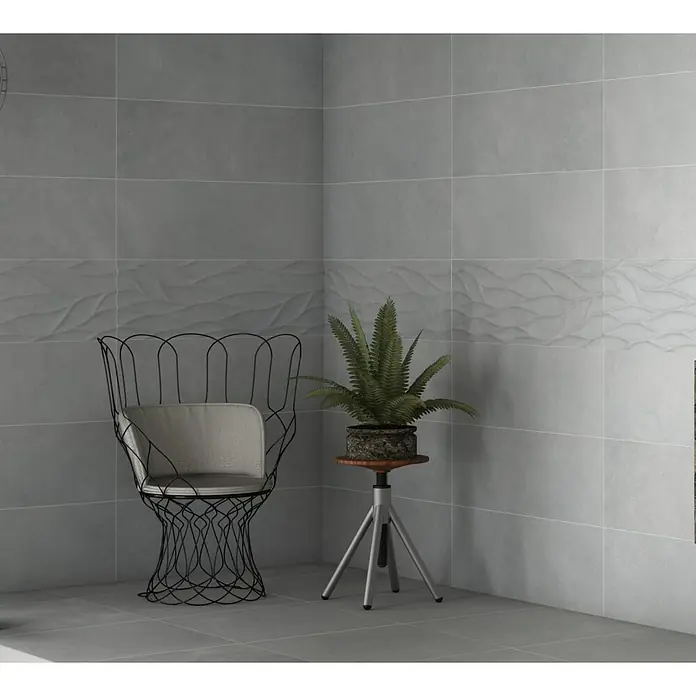 Revestimiento de pared Step - 30 x 90 cm, Gris, Rectificado - Elegantes azulejos grises con un patrón ondulado en la pared, acentuados por una silla de estilo y una planta en maceta. Los azulejos dan un toque moderno al espacio.