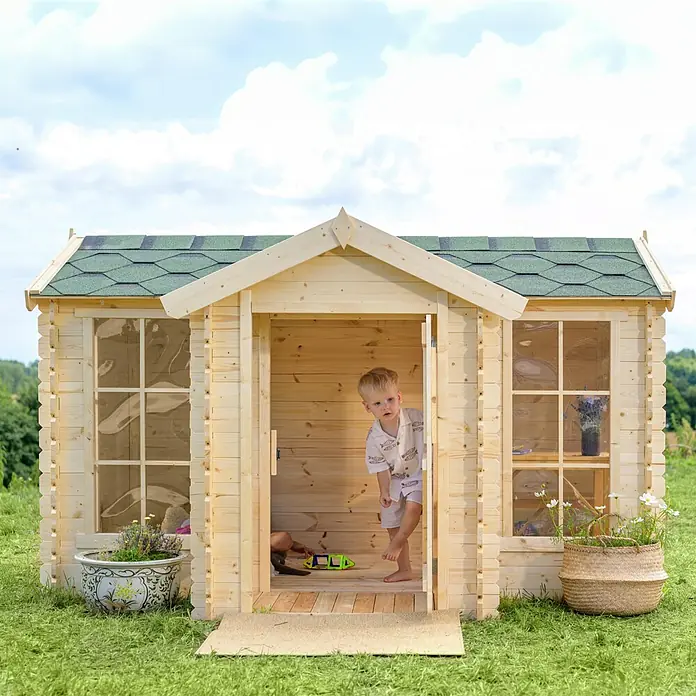 Timbela Spielhaus - L x B x H: 187 x 241 x 151 cm, Holz, Natur - Ein kleines Kind steht in einem Holzspielhaus mit grünen Schindeln und Blumenkästen.