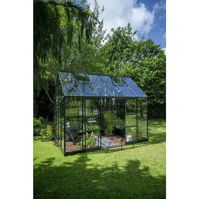Halls Gewächshaus Icon Planthouse - Außenmaß inkl. Dachüberstand (B x T): 379,1 x 254,7 cm, Material Seitenwand: Glas, 3 mm, Grün - Gewächshaus im Garten. Das Gewächshaus ist aus Glas und Metall gefertigt und bietet viel Platz für Pflanzen. Die Umgebung ist grün und idyllisch.