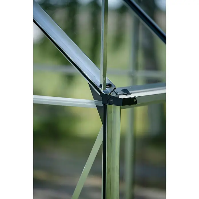 Halls Gewächshaus Icon 6 Blankglas - Außenmaß inkl. Dachüberstand (B x T): 192,5 x 316,9 cm, Material Seitenwand: Glas, 3 mm, Aluminium - Nahaufnahme eines Gewächshausrahmens mit silbernen Metallstreben und schwarzen Verbindungselementen vor grünem Hintergrund.