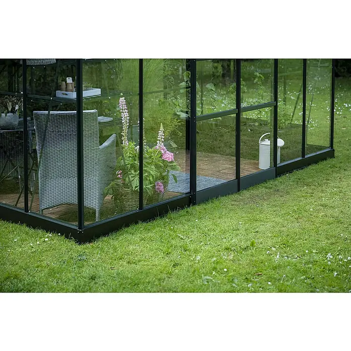 Halls Gewächshaus Icon Planthouse - Außenmaß inkl. Dachüberstand (B x T): 379,1 x 254,7 cm, Material Seitenwand: Glas, 3 mm, Grün - Nahaufnahme eines Gewächshauses mit Pflanzen und Gartenmöbeln, die eine ruhige und einladende Atmosphäre schaffen.
