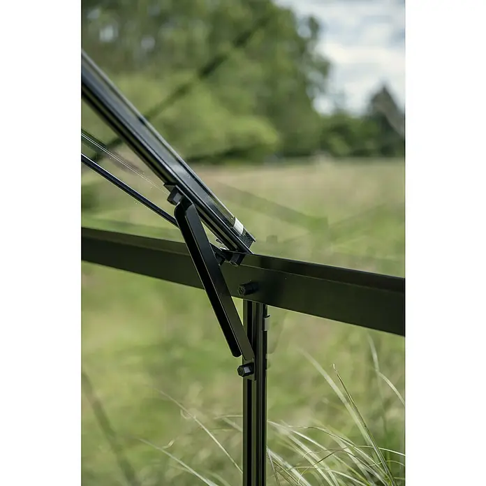 Halls Gewächshaus Icon Gardenhouse - Außenmaß inkl. Dachüberstand (B x T): 321,7 x 319,4 cm, Material Seitenwand: Glas, 3 mm, Schwarz - Nahaufnahme eines schwarzen Gewächshausfensters mit Öffnungsmechanismus vor grünem Hintergrund.