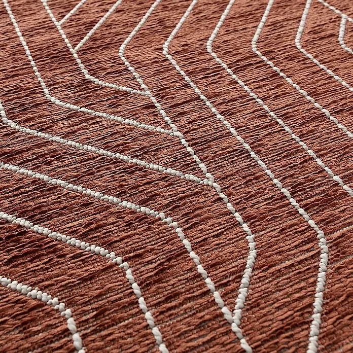 Dekoria Flachgewebeteppich - kupfer, 170 x 120 cm - Nahaufnahme eines texturierten, terrakottafarbenen Teppichs mit geometrischen, weißen Akzenten. Das Design erzeugt ein stilvolles Muster.