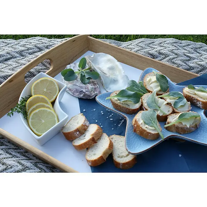 Blu Bio Austernpflanze - Mertensia maritima, Topfgröße: 12 cm - Auf einem Holztablett befinden sich Austern, Zitronenscheiben und mit Butter bestrichene Brotscheiben mit Salatblättern für eine köstliche Vorspeise.