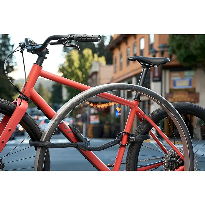 Abus Kettenschloss 1806 Infinity Loop - Länge: 140 cm, Stärke: 6 mm - Nahaufnahme von zwei roten Fahrrädern, die mit einem schwarzen ABUS-Kettenschloss an einem Fahrradständer gesichert sind.