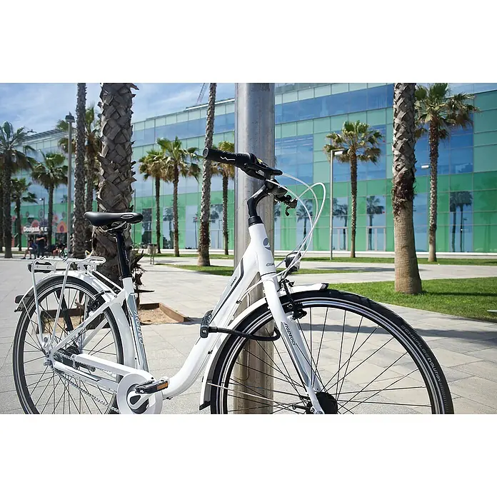 Abus Panzerkabelschloss Microflex 6615K - Länge: 85 cm - Nahaufnahme eines weißen Giant Argenco Citybikes mit U-Schloss an einem Pfosten, Palmen und einem Gebäude im Hintergrund.