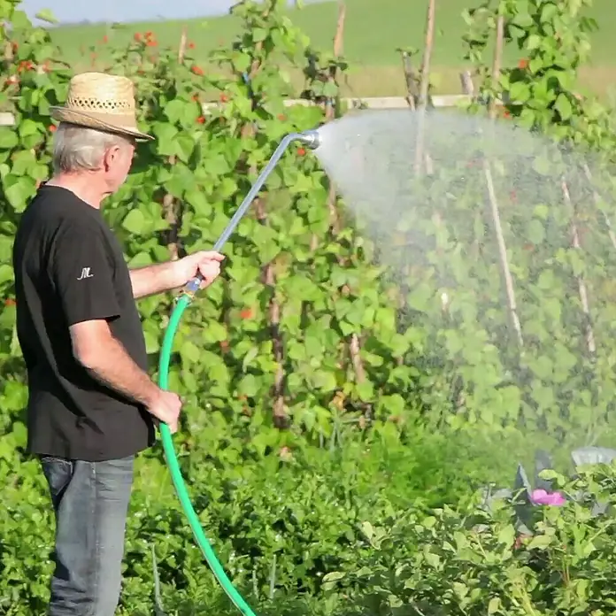Güde Drucktauchpumpe GDT 1200 I - 1.200 W, Max. Fördermenge: 6.000 l/h - Ein Mann mit Hut bewässert seinen Garten mit einem praktischen Gartenschlauch mit Sprühkopf. Ideal für die Bewässerung empfindlicher Pflanzen.