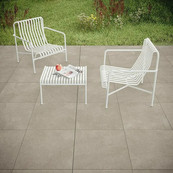 Terrassenfliese Stoneline - 60 x 60 x 2 cm, Beige/Grau, Matt - Gartenszene mit weißen Gartenmöbeln auf Fliesenboden mit einem Apfel, einer Zeitung und einer Brille auf dem Tisch.