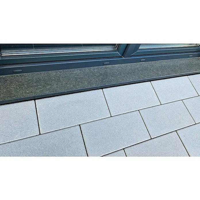 Christoph Pflasterstein - Kristall-Grau, 40 x 20 x 6 cm, Rechteck - Nahaufnahme von grauen Pflastersteinen, die eine Terrasse oder einen Gehweg bilden, angrenzend an eine dunkle Fensterbank.