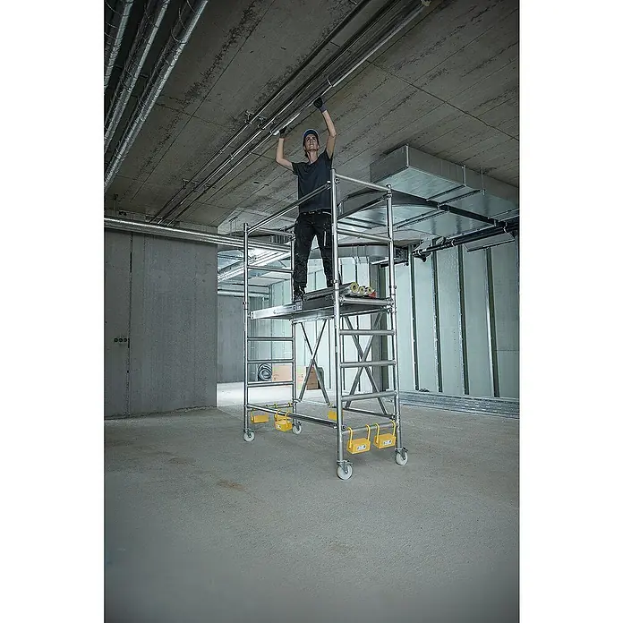 Proregal Klappgerüst mit Ausbaueinheit -  - Silbernes Rollgerüst mit Arbeiter bei der Rohrinstallation in einem Gebäude.