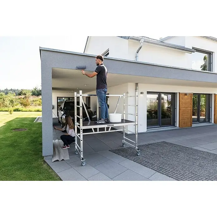 Proregal Klappgerüst türengängig -  - Mobiles Aluminium-Rollgerüst mit dunkler Plattform, von einem Mann zum Streichen einer Hauswand genutzt. Eine Frau streicht den unteren Bereich.