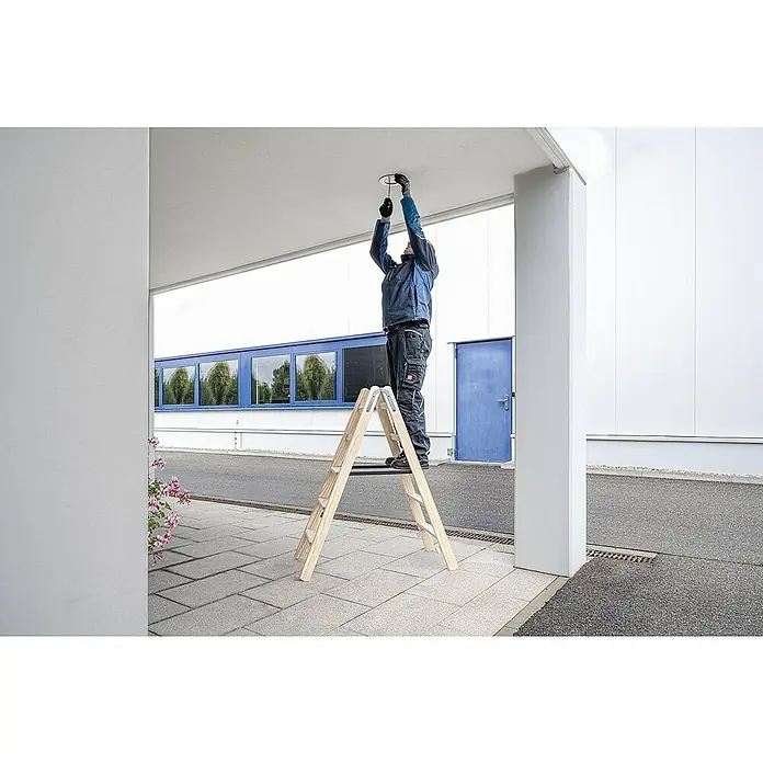 Proregal Doppel-Stehleiter mit 16 Stufen - Anzahl Tritte: 16 Stk., Arbeitshöhe: 3.410 mm, Belastbarkeit: 150 kg, Holz - Hölzerne Stehleiter in Gebrauch, die eine Person beim Anbringen einer Deckenleuchte stützt.