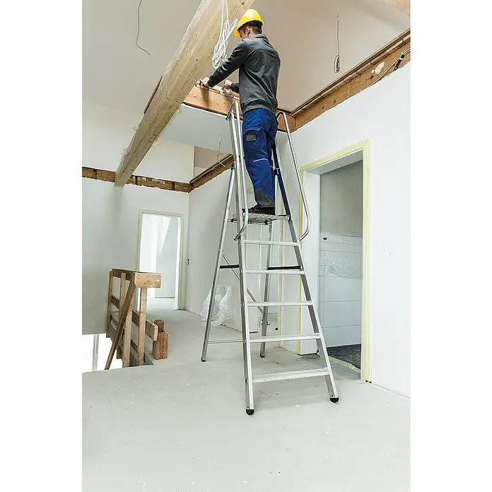 Proregal Stehleiter mit 7 Stufen - Anzahl Tritte: 7 Stk., Arbeitshöhe: 3.600 mm, Belastbarkeit: 150 kg, Aluminium - Silberne Aluminium-Arbeitsplattformleiter mit Handläufen, von einem Arbeiter zur Deckenmontage verwendet.