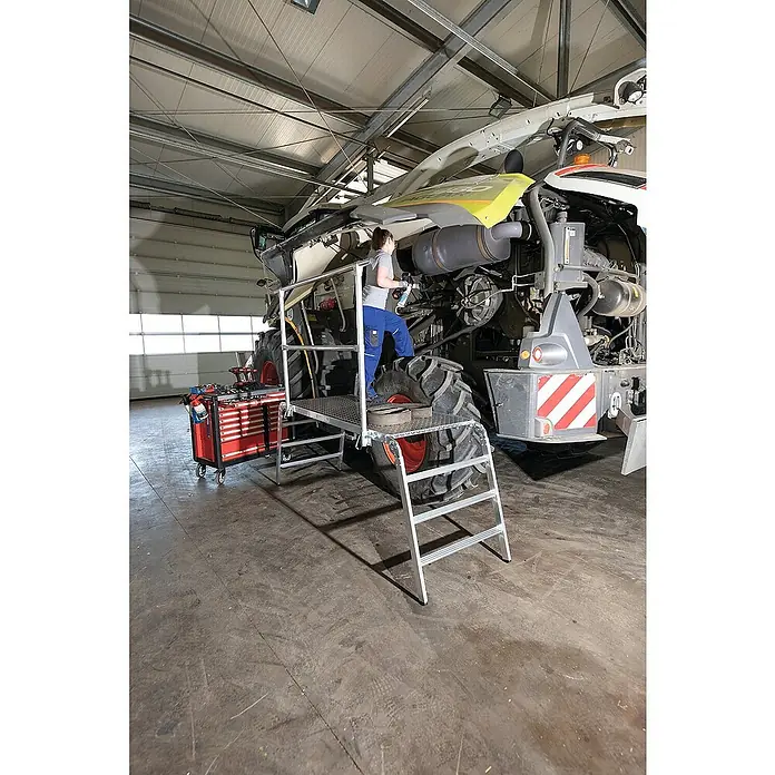 Proregal Arbeitsplattform klappbar - Arbeitshöhe: 2.980 mm, Belastbarkeit: 500 kg, Aluminium - Aluminium-Arbeitsplattform mit Stufen, von einem Techniker zur Reparatur einer großen Landmaschine genutzt.