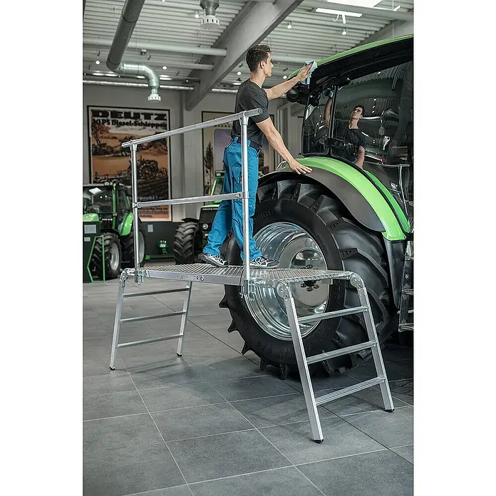 Proregal Arbeitsplattform klappbar - Arbeitshöhe: 2.980 mm, Belastbarkeit: 500 kg, Aluminium - Silberne Arbeitsplattform mit Geländer, die es einem Mann ermöglicht, die Kabine eines großen grünen Traktors sicher zu reinigen.