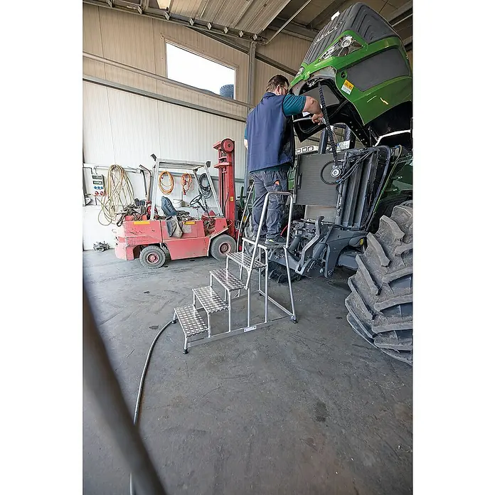 Proregal Treppenpodest Arbeitspodest starr mit 3 Stufen - Anzahl Tritte: 3 Stk., Arbeitshöhe: 2.600 mm, Belastbarkeit: 150 kg, Aluminium - Mann auf mehrstufiger Aluminium-Arbeitsplattform, der den Motor eines großen Traktors in einer Werkstatt wartet.