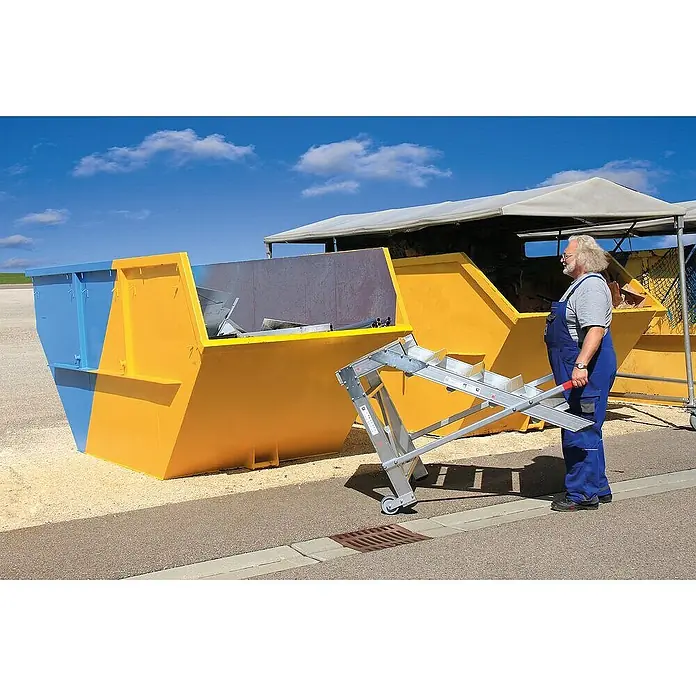 Proregal Treppenpodest Arbeitspodest fahrbar - Anzahl Tritte: 2 Stk., Arbeitshöhe: 2.400 mm, Belastbarkeit: 200 kg, Aluminium - Mann bereitet eine silberne, fahrbare Laderutsche für große gelb-blaue Abfallcontainer vor.
