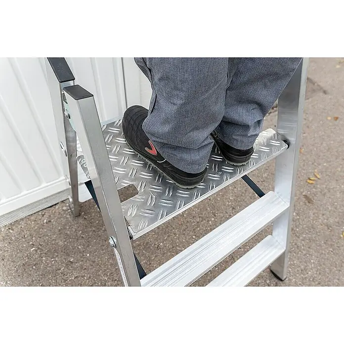 Proregal Doppel-Klapptritt beidseitig begehbar - Anzahl Tritte: 3 Stk., Arbeitshöhe: 2.730 mm, Belastbarkeit: 150 kg, Aluminium - Person steht auf den rutschfesten geriffelten Aluminiumstufen einer silbernen Leiter.