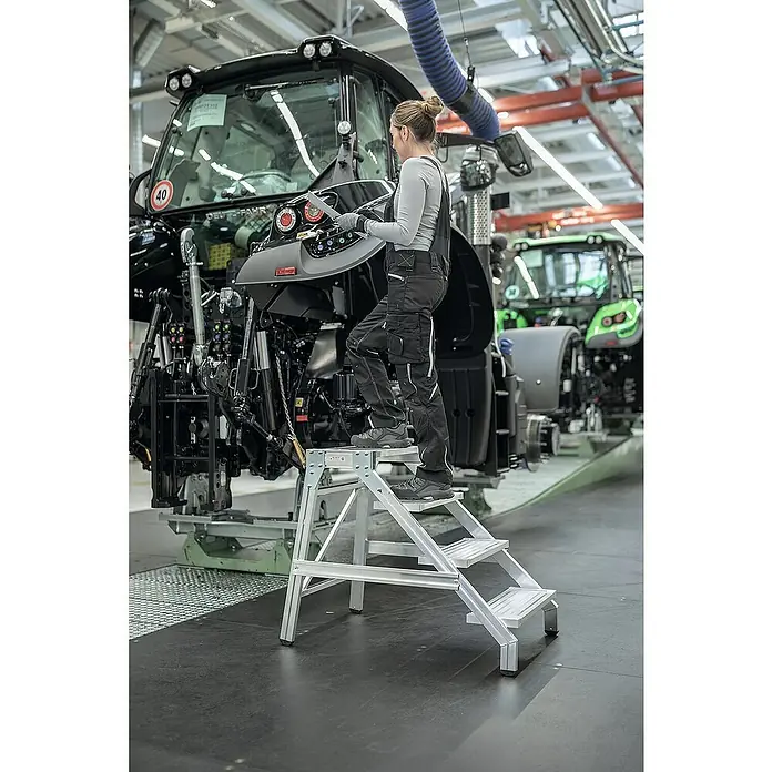 Proregal Treppenpodest Montagetritt mit 4 Stufen - Anzahl Tritte: 4 Stk., Arbeitshöhe: 2.800 mm, Belastbarkeit: 300 kg, Aluminium - Silberne Aluminium-Trittleiter, die einer Person stabilen Zugang bei der Arbeit an einer großen Maschine bietet.