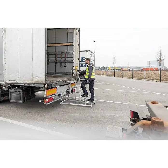 Proregal Treppenpodest Arbeitspodest starr mit 5 Stufen - Anzahl Tritte: 5 Stk., Arbeitshöhe: 3.000 mm, Belastbarkeit: 150 kg, Aluminium - Silberne Aluminium-Treppenleiter, von einem Arbeiter zum sicheren Zugang zum LKW-Auflieger verwendet.