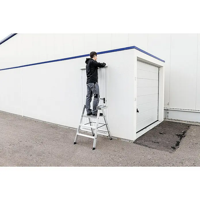 Proregal Doppel-Klapptritt beidseitig begehbar - Anzahl Tritte: 4 Stk., Arbeitshöhe: 2.990 mm, Belastbarkeit: 150 kg, Aluminium - Eine Person steht auf einer silbernen Aluminium-Klapptritt, um etwas über einer Tür anzupassen. Die robuste Trittleiter ermöglicht den Zugang zu Aufgaben.