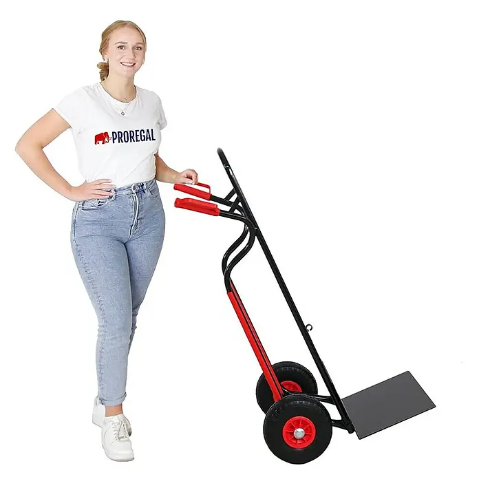Proregal Sackkarre RAGNAR mit klappbarer XXL Schaufel & PU-Bereifung - Stahl, Traglast: 250 kg - Eine Frau demonstriert eine schwarze und rote Sackkarre mit schwarzen Rädern.