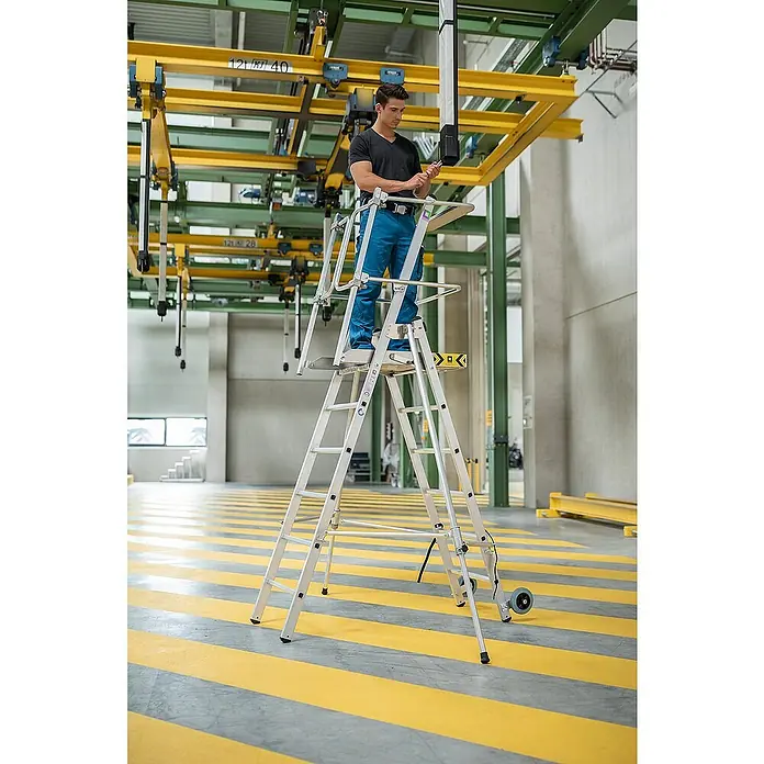 Proregal Stehleiter Plattformleiter Flexstep - Anzahl Tritte: 4 Stk., Arbeitshöhe: 3.000 mm, Belastbarkeit: 150 kg, Aluminium - Mann auf einer silbernen Aluminium-Arbeitsplattform/Leiter in einer Industriehalle, arbeitet in der Höhe mit einem Werkzeug.