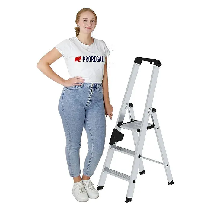 Proregal Stehleiter einseitig begehbar - Anzahl Tritte: 3 Stk., Arbeitshöhe: 2.700 mm, Belastbarkeit: 150 kg, Aluminium - Silberne Klapptrittleiter mit schwarzen Akzenten, neben einer Frau zur Größenreferenz gezeigt. Sie hat eine obere Plattform und zwei Stufen.