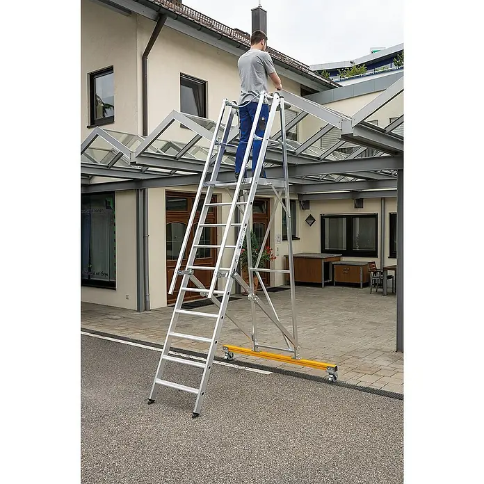 Proregal Stehleiter Plattformleiter klappbar und fahrbar - Anzahl Tritte: 14 Stk., Arbeitshöhe: 5.250 mm, Belastbarkeit: 150 kg, Aluminium - Silbernes Aluminium-Mehrzweckgerüstsystem mit einem Mann auf der Plattform, der an einem Glasvordach arbeitet.