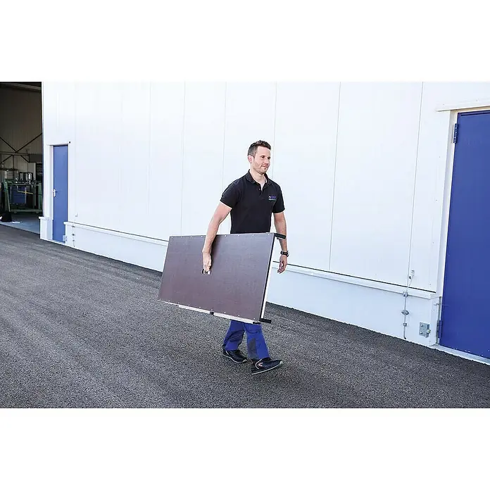 Proregal Treppenpodest Arbeitsdiele klappbar - Arbeitshöhe: 2.700 mm, Belastbarkeit: 300 kg, Aluminium - Mann trägt eine dunkelbraune Klapptafel mit Griff, was ihre Portabilität und Transportfreundlichkeit demonstriert.