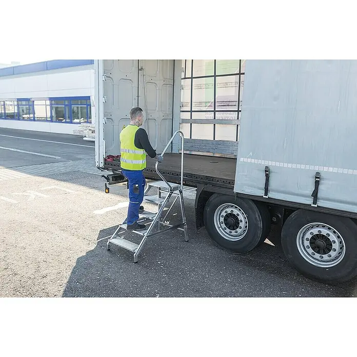 Proregal Treppenpodest Montagetritt mit Handlauf mit Handlauf - Anzahl Tritte: 4 Stk., Arbeitshöhe: 2.800 mm, Belastbarkeit: 300 kg, Aluminium - Silberne Aluminium-Arbeitstreppe mit Geländer, von einem Arbeiter zum sicheren Betreten eines LKW-Anhängers verwendet.