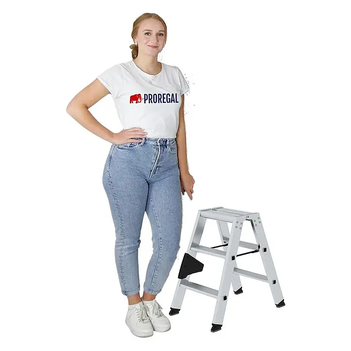 Proregal Doppel-Stehleiter beidseitig begehbar - Anzahl Tritte: 6 Stk., Arbeitshöhe: 2.200 mm, Belastbarkeit: 150 kg, Aluminium - Silberner Aluminium-2-Stufen-Klapphocker neben einer Frau, die seine kompakte Größe zeigt.