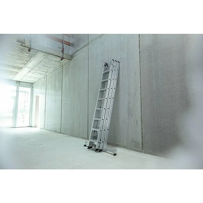 Proregal Mehrzweckleiter 3-teilig - Anzahl Tritte: 18 Stk., Arbeitshöhe: 5.200 mm, Belastbarkeit: 150 kg, Aluminium - Silberne Aluminium-Ausziehleiter lehnt an einer Betonwand in einem Rohbau.