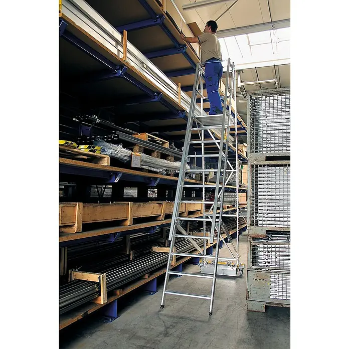 Proregal Stehleiter Plattformleiter klappbar mit schmalem Fahrwerk - Anzahl Tritte: 6 Stk., Arbeitshöhe: 3.400 mm, Belastbarkeit: 150 kg, Aluminium - Silberne Aluminium-Arbeitsplattform mit Mann, der in einem Lager hohe Regale erreicht.