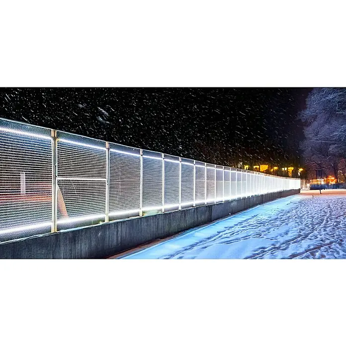 Müller-Licht LED-Stripes Power - 25 m, Tageslichtweiß, 6.500 K, 25.000 lm, 290 W - Eine lange Lärmschutzwand mit LED-Beleuchtung, die eine Schneebedeckte Straße in einer dunklen Winternacht erhellt.