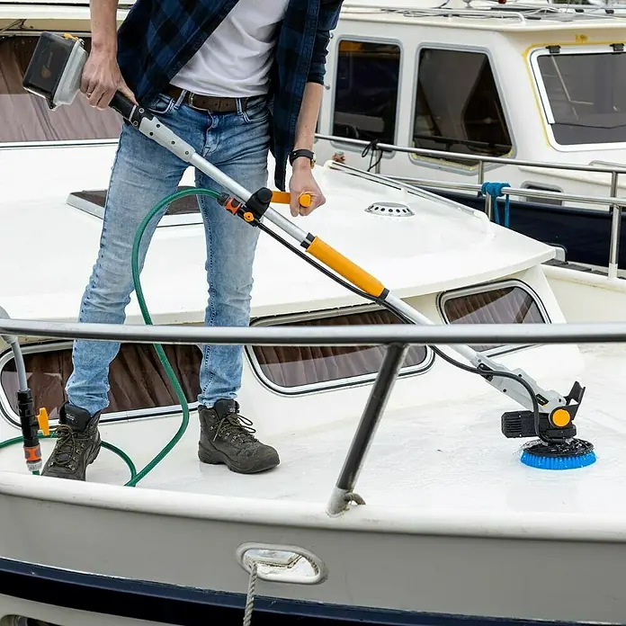Batavia Maxxpack Akku-Reinigungsbürste Twin Brush V1 - 18 V, 1 Akku, 2 Ah - Eine Person benutzt eine Reinigungsbürste mit Stiel, um ein Boot zu reinigen. Die Bürste hat einen blauen Bürstenkopf und ist mit einem Schlauch verbunden.