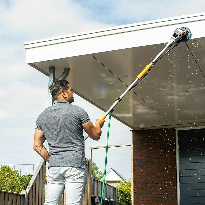 Batavia Maxxpack Verlängerungsstiel - Passend für: Batavia Maxxpack Akku-Reinigungsbürste Twin Brush V1, 80 cm - 240 cm - Ein Mann benutzt eine rotierende Bürste mit Teleskopstiel, um eine Hauswand zu reinigen, was die Reinigungsleistung und Reichweite des Produkts hervorhebt.