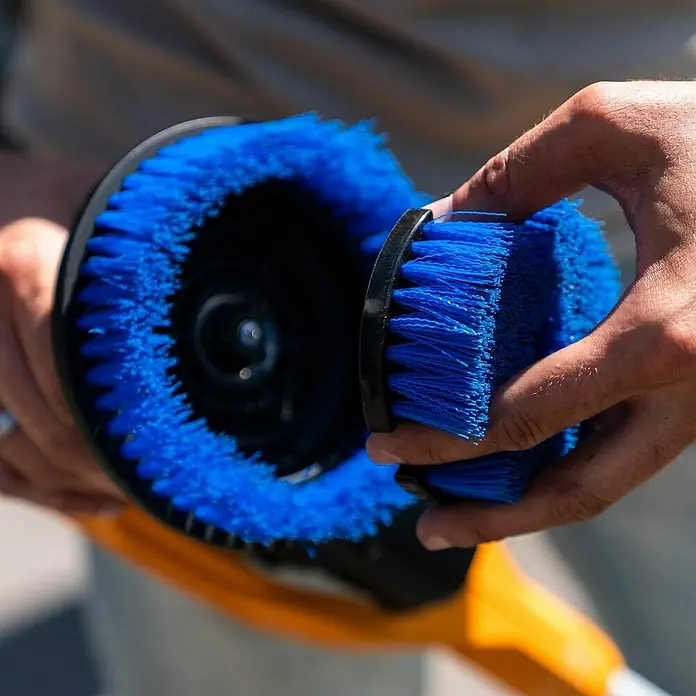 Batavia Akku-Reinigungsbürste Twin Brush Compact - 12 V, Ohne Akku - Eine Nahaufnahme einer blauen Bürste mit schwarzem Griff, gehalten von einer Person, die die Details und Textur der Bürste hervorhebt.