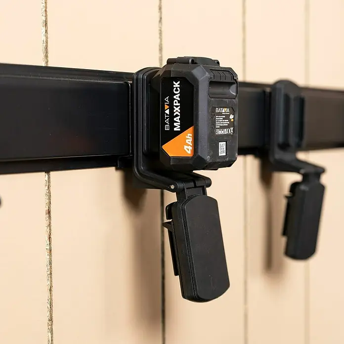 Batavia Maxxclick Systemhalter Click & Go Rail - Länge: 58 cm - Ein Maxxpack 4Ah Akku von Batavia hängt an einer schwarzen Akkuaufhängung an einer beigen Wand.