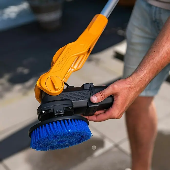 Batavia Akku-Reinigungsbürste Twin Brush Compact - 12 V, Ohne Akku - Das Bild zeigt eine gelb-schwarze Bürste mit blauem Bürstenkopf. Das Gerät wird von einer Hand gehalten und ist für Reinigungsarbeiten im Außenbereich gedacht.