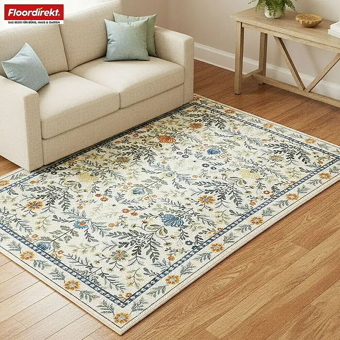 Floordirekt Kurzflorteppich Orientalis 160 x 230 cm - Ecru, 230 x 160 cm - Cremefarbener floraler Teppich mit blauen, orangefarbenen und grünen Pflanzenmustern, unter einem Sofa auf Holzfußboden.