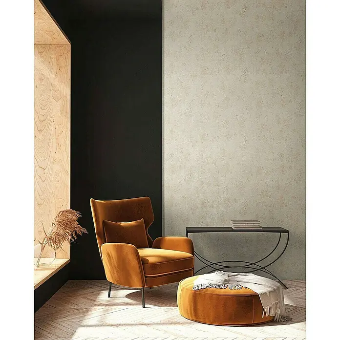 Tadessi Vliestapete M1-No.4041 - Creme, Steinoptik, 10,05 x 0,53 m - Ein bernsteinfarbener Samtsessel und passender Hocker bilden eine gemütliche Sitzecke in einem modernen Raum.