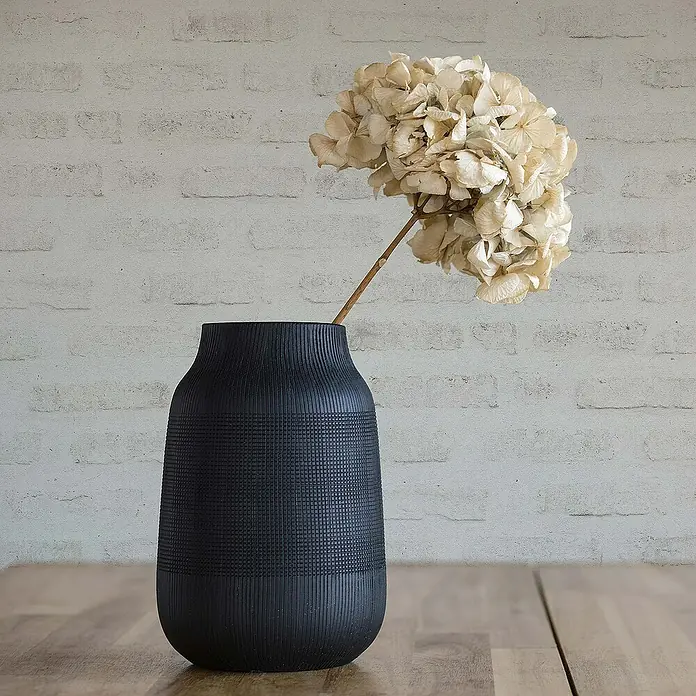 Tadessi Vliestapete M1-No.418 - Grau, Steinoptik, 10,05 x 0,53 m - Schwarze strukturierte Vase mit Rillen- und Gittermuster, die eine Trockenblume hält.