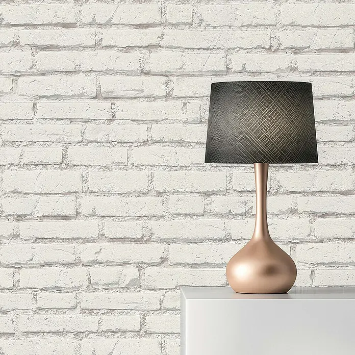 Tadessi Vliestapete M1-No.53 - Grau, Steinoptik, 10,05 x 0,53 m - Roségoldene Tischlampe mit dunklem, texturiertem Schirm auf weißer Oberfläche vor weißer Ziegelwand.