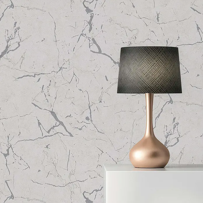 Tadessi Vliestapete M1-No.603 - Grau, Steinoptik, 10,05 x 0,53 m - Eine moderne Tischlampe mit dunklem, gemustertem Schirm und glänzendem roségoldenem Fuß auf einem weißen Regal vor einer Marmorwand.